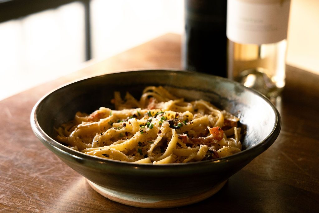 A bowl of fresh pasta with wine, in warm window light