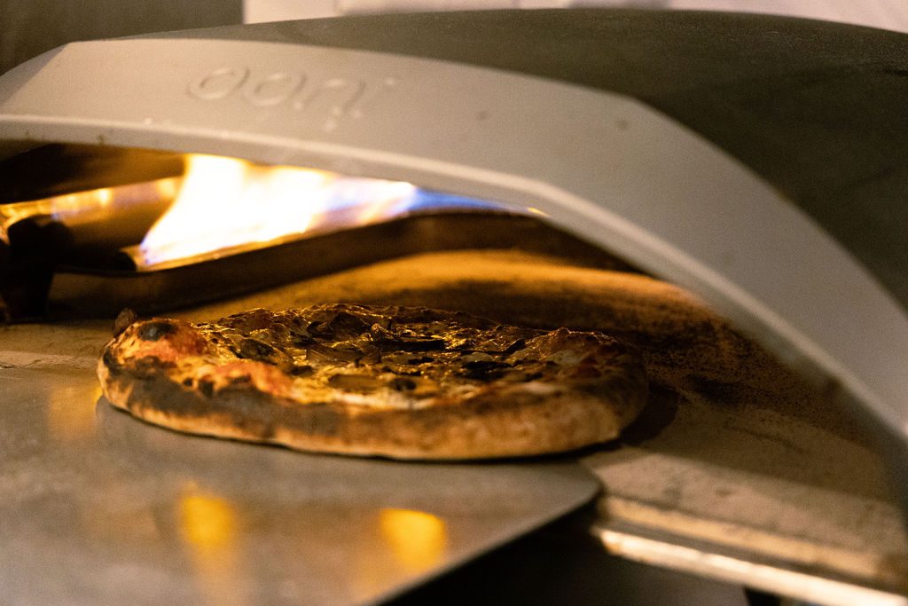 A pizza baking in the flame of a wood-fired oven